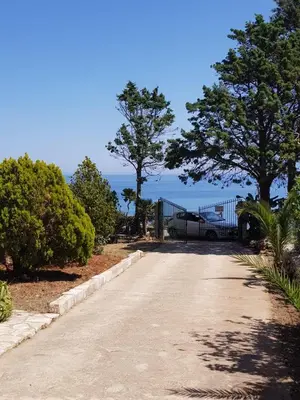 a driveway with a gate and trees and the ocean at Appartamenti Cala Rossa (Antonella) in Castellammare del Golfo