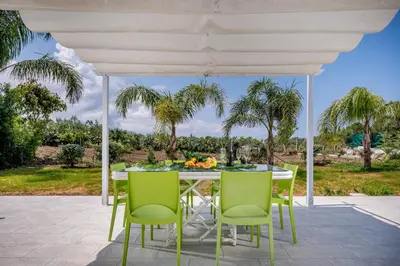 a table and chairs on a patio with palm trees at Villa Sikelia in Alcamo