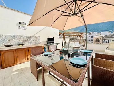 a table with glasses and an umbrella on a balcony at Appartamento Alexa in Castellammare del Golfo