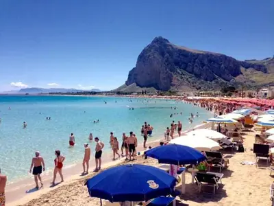 a group of people on a beach with blue umbrellas at Il Giardino del Sol in San Vito lo Capo