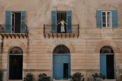a woman in a dress on a balcony of a building at Tonnara Foderà di Magazzinazzi in Alcamo
