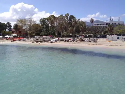 a beach with blue water and buildings and trees at La casetta di rosario mondello in Palermo