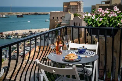 a table with a plate of food and wine glasses on a balcony at La suite del Golfo in Castellammare del Golfo