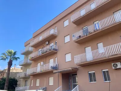 a building with white balconies and a palm tree at Easy Room Holiday in Castellammare del Golfo