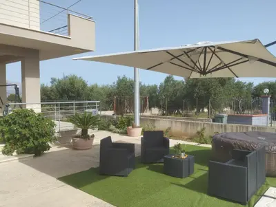 a patio with chairs and an umbrella and grass at Casa vacanze Elisir Del Golfo in Alcamo