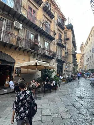 a woman walking down a street with people sitting at tables at La Volta di Gatto in Palermo