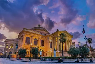 a large yellow building with palm trees in front of it at Le Trottole Apartment in Palermo