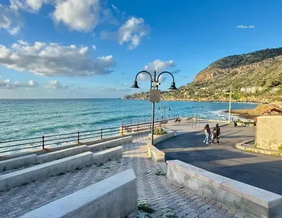 two people walking down a sidewalk next to the ocean at TOURIST HOUSE Le casette di Sofì in Bagheria