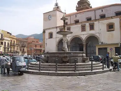 a fountain in front of a building with a clock at casaafauka in Carini