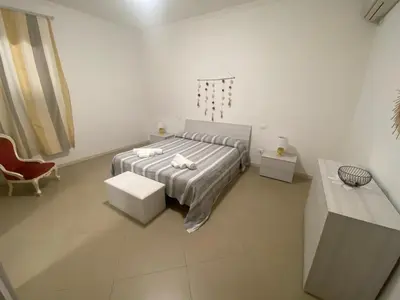 a white bedroom with a bed and a chair at Casa Ciccio in Cinisi