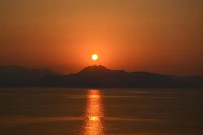 a sunset over the water with a mountain in the background at Calipso in Bagheria