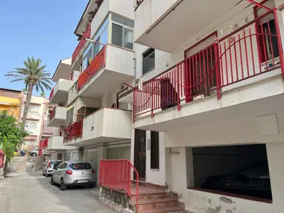 a building with red balconies and cars parked on a street at Lo Scorcio sul Mare by Holiday World in Isola delle Femmine