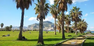 a park with palm trees and people sitting in the grass at Sunny Home in Palermo