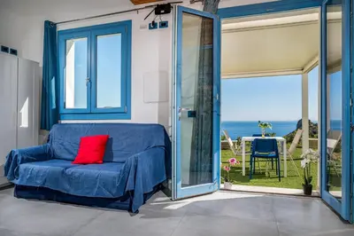 a blue couch with a red pillow on it in a room with glass doors at Villa Holidays Vista Torre Bennistra in Scopello in Scopello