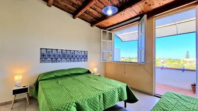 a bedroom with a green bed and a large window at Appartamenti Amagea in Scopello