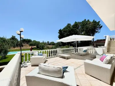 a patio with white furniture and an umbrella at Villa Rachele con piscina in Balestrate