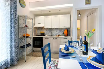 a kitchen with a table with blue chairs and white cabinets at Appartamento Dolceluna in San Vito lo Capo
