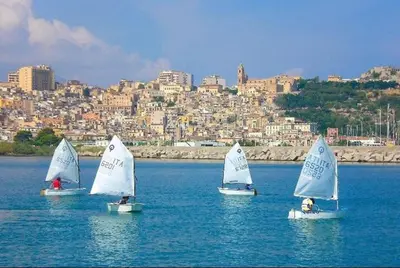 four small sailboats in the water with a city in the background at Sicilian Apartment in Termini Imerese