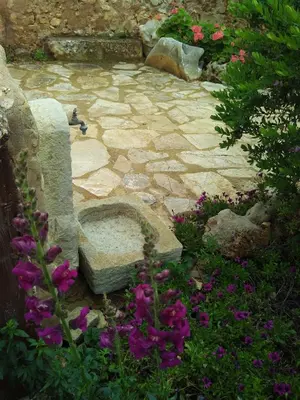 a stone patio with purple flowers and a stone bench at Baglio Poma in Castelluzzo