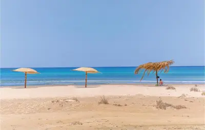 three straw umbrellas on a beach with the ocean at Awesome Home In Partinico With Wi-Fi in Partinico