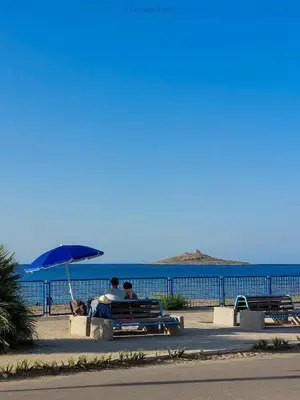 two people sitting on a bench under an umbrella at Il Cortile Isola Casa Vacanze in Isola delle Femmine