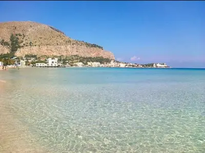 a beach with clear water and a mountain in the background at casa giorgia mondello in Palermo