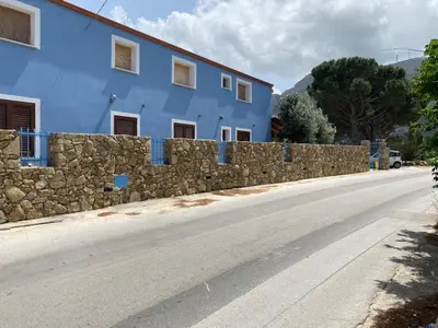 a blue building with a stone wall next to a road at B&B Pelagos in Castellammare del Golfo