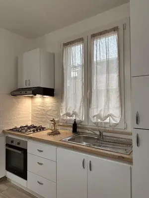 a kitchen with white cabinets and a sink and two windows at Casa Andrew in Terrasini