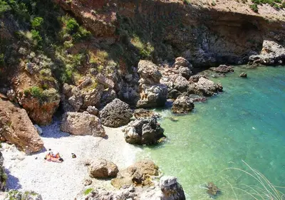 a beach with rocks and water and people in the water at Casa vacanza la finestra sul porto in Castellammare del Golfo
