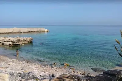 a man standing in the water on a rocky beach at Casa Gabriele in Palermo