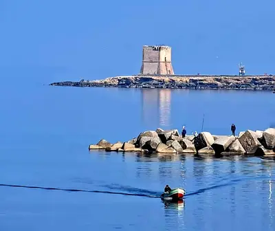 a man in a boat in the water with a lighthouse in the background at Villa Antonio in Cinisi