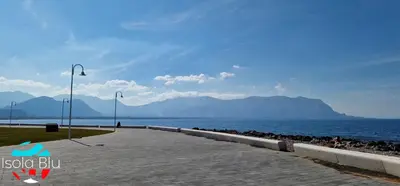 a walkway next to a body of water with mountains at Isola Blu Casa a pochi passi dal mare in Isola delle Femmine