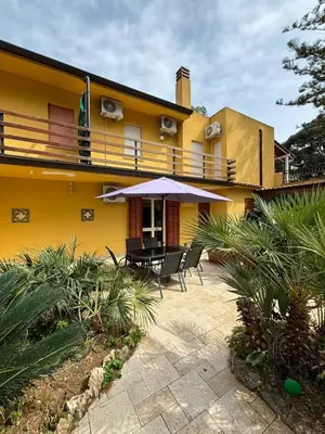 a yellow house with a patio with chairs and an umbrella at Villa Chifeci Scopello - Appartamento La Zàgara in Scopello