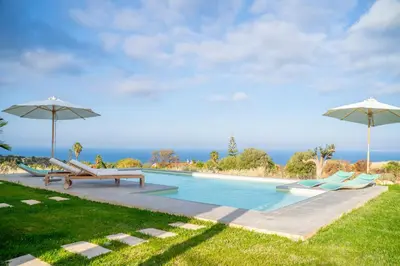 a swimming pool with two umbrellas and some chairs and a pool at Villa Majestatis con piscina privata in Scopello