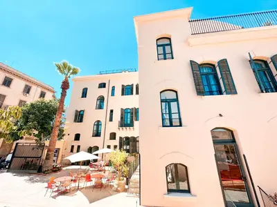 a white building with tables and chairs next to a palm tree at Ostello Bello Palermo in Palermo