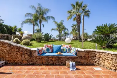 a blue couch on a stone wall with palm trees at Verosicily Villa Barcellona in Terrasini
