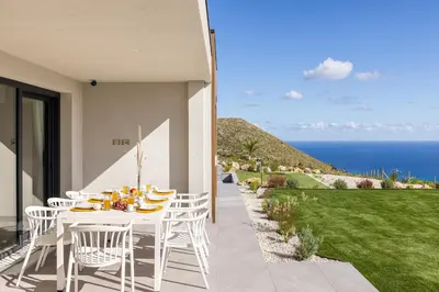 a white table and chairs on a patio with the ocean at Villa Adler Nature&Relax in Scopello