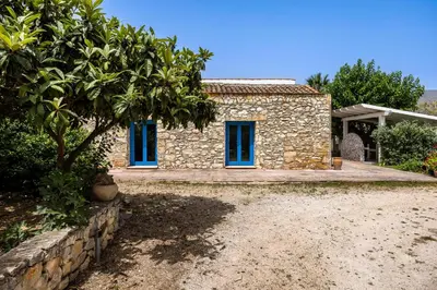 a stone house with blue windows and a tree at Villa Celeste in Castellammare del Golfo