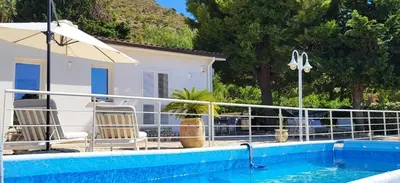 a pool with chairs and an umbrella next to a house at Villa Ballerina Bianca in Scopello