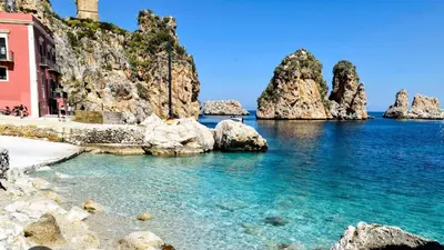 a beach with rocks in the water and a pink building at La Casetta di Nino in Castellammare del Golfo