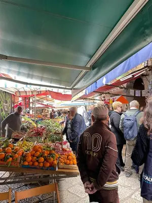 a group of people standing around a market with fruits and vegetables at Studio 29 in Palermo