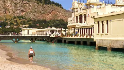 a woman walking on the beach next to a bridge at Lo scarrozzo room in Palermo
