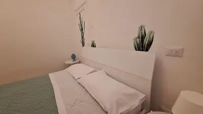 a white bedroom with a bed and a plant at La Casa All'Angolo in Altavilla Milicia