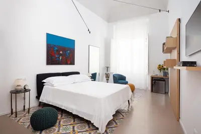 a white bedroom with a bed and a blue chair at Piano Alloro in Palermo