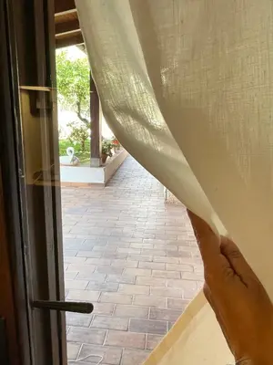 a hand is holding a curtain in front of a door at Baglio Sammartano ROOM&TOUR in Castelluzzo