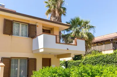 a house with a balcony and palm trees at Isola Suite in Isola delle Femmine