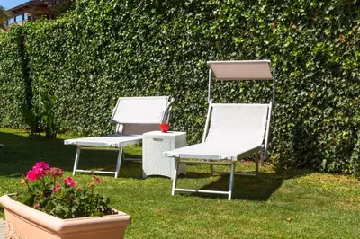 two white chairs sitting in the grass next to a hedge at Isola Suite in Isola delle Femmine