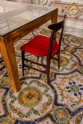 a wooden table with a red chair in front of a mosaic floor at Palazzo Sant'Isidoro by DomuSicily in Palermo