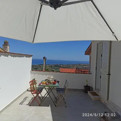 a patio with a table and chairs and a white umbrella at Mediterraneo Rooms in Castellammare del Golfo