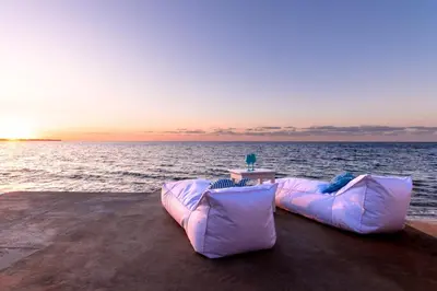 a couch sitting next to the ocean at sunset at Vista Mare by DomuSicily in Cinisi